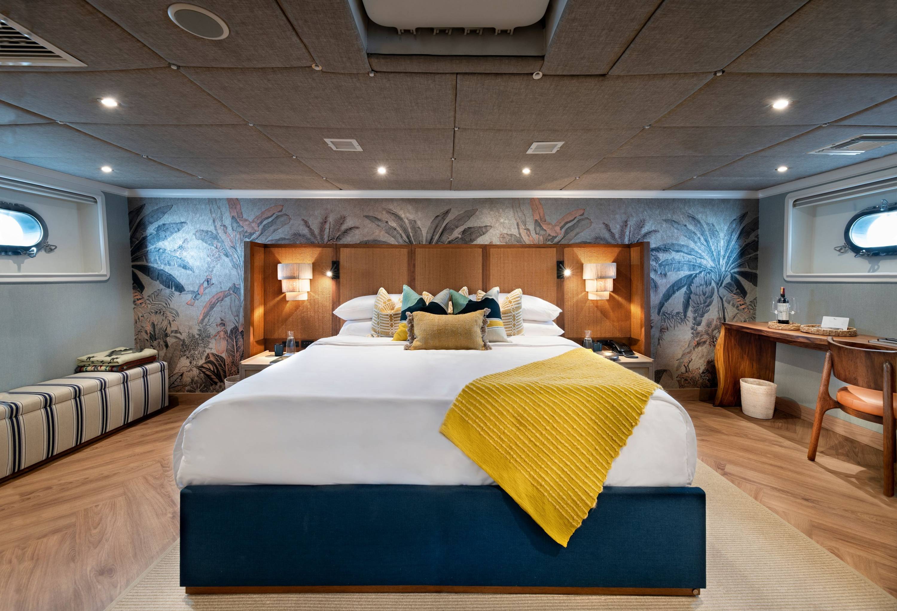 Eleganz auf See Stilvoll eingerichtete Luxuskabine mit Kingsize-Bett, Naturholz-Schreibtisch und tropischer Wandgestaltung an Bord einer Yacht.