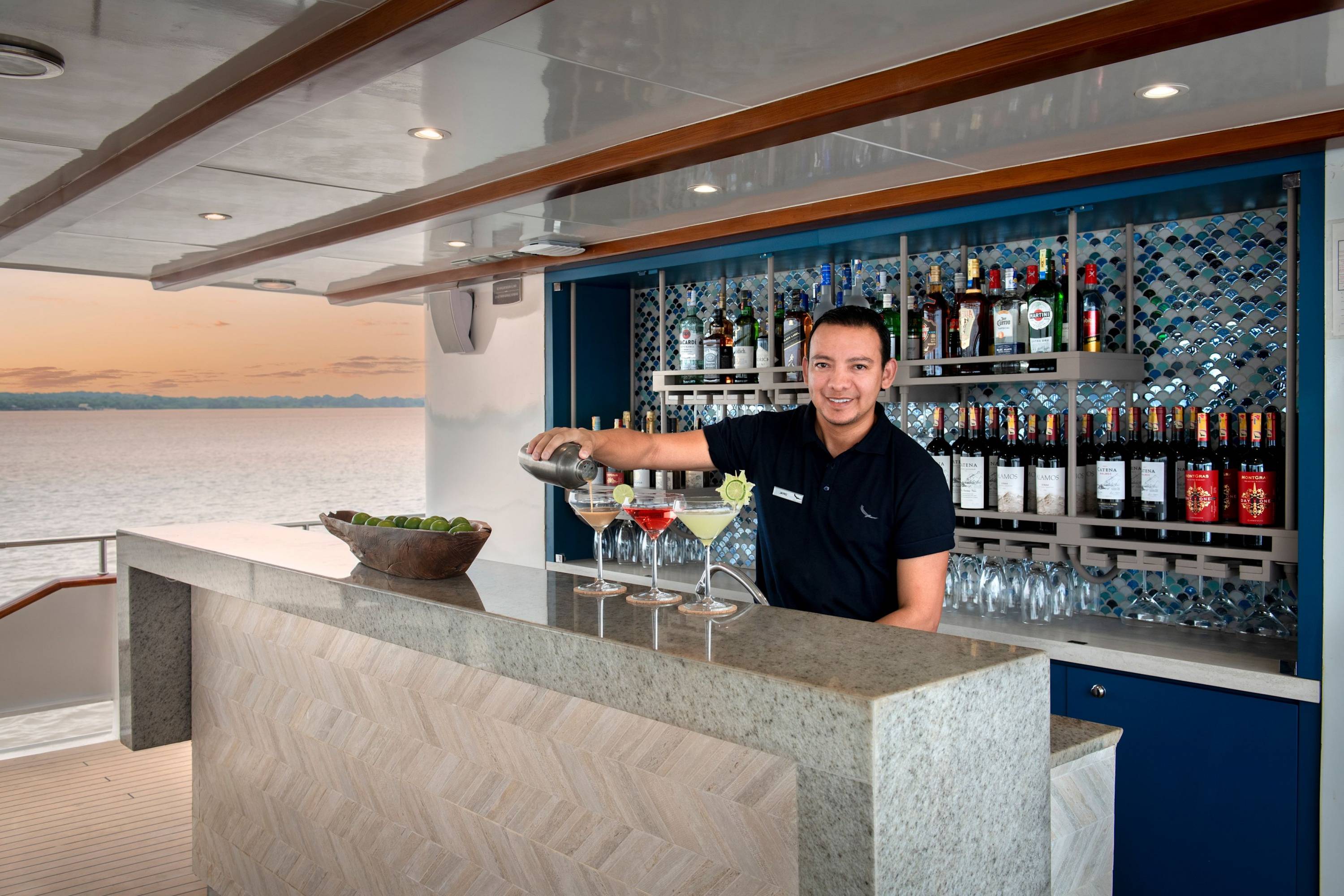 Sundowner mit Aussicht Barkeeper auf der Yacht „Galapagos Explorer“ serviert farbenfrohe Cocktails an einer stilvollen Bar bei Sonnenuntergang.