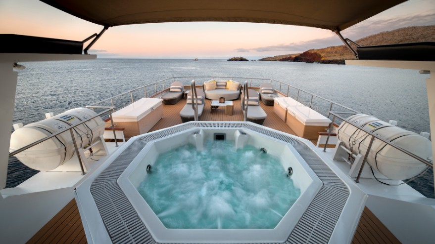 Entspannung mit Aussicht Luxuriöser Whirlpool auf dem Oberdeck einer Yacht, mit Blick auf das Meer und eine felsige Galapagos-Insel im Sonnenuntergang.