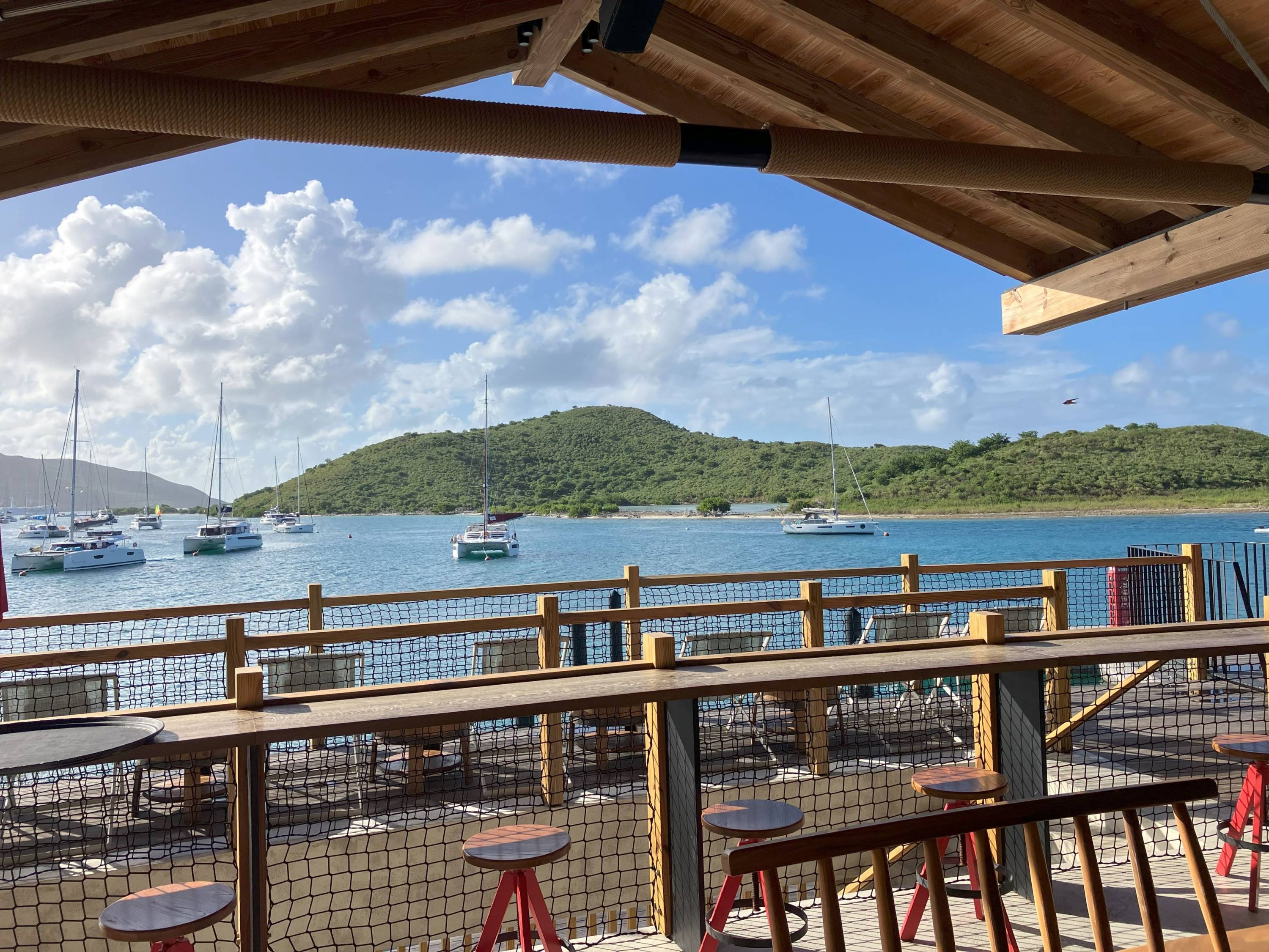 Blick von einer offenen Strandbar Saba Rock auf eine tropische Bucht mit mehreren ankernden Katamaranen.