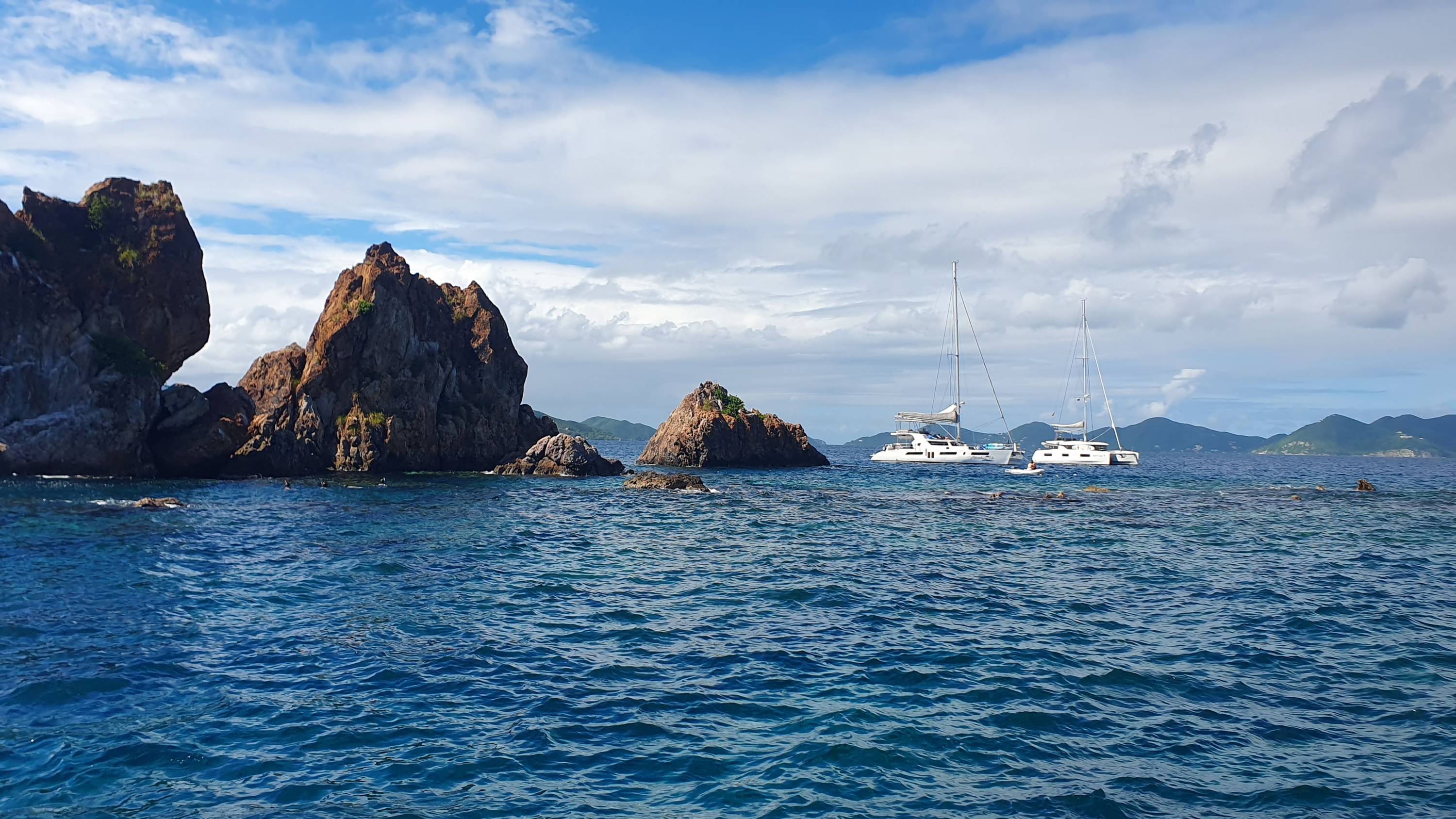 Zwei Katamarane ankern vor den felsigen Formationen bei Pelican Island in den British Virgin Islands, während Schnorchler das klare Wasser erkunden.