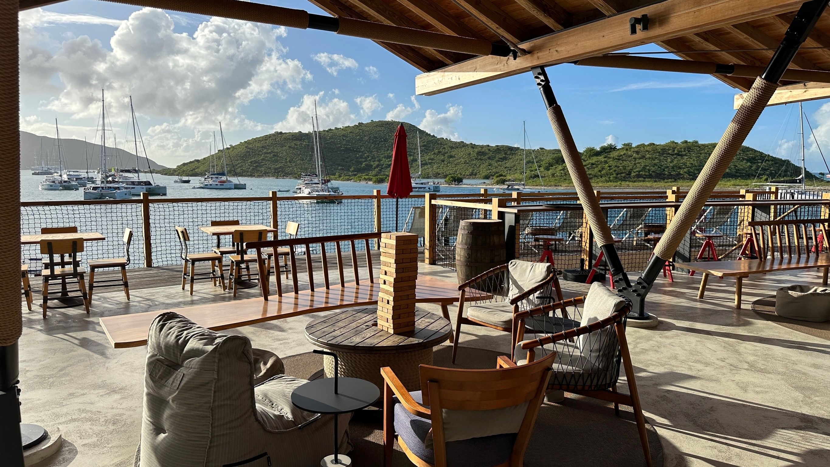 Moderne offene Bar mit Holzmöbeln und Blick auf eine ruhige Bucht mit vielen ankernden Segel- und Katamaran-Yachten