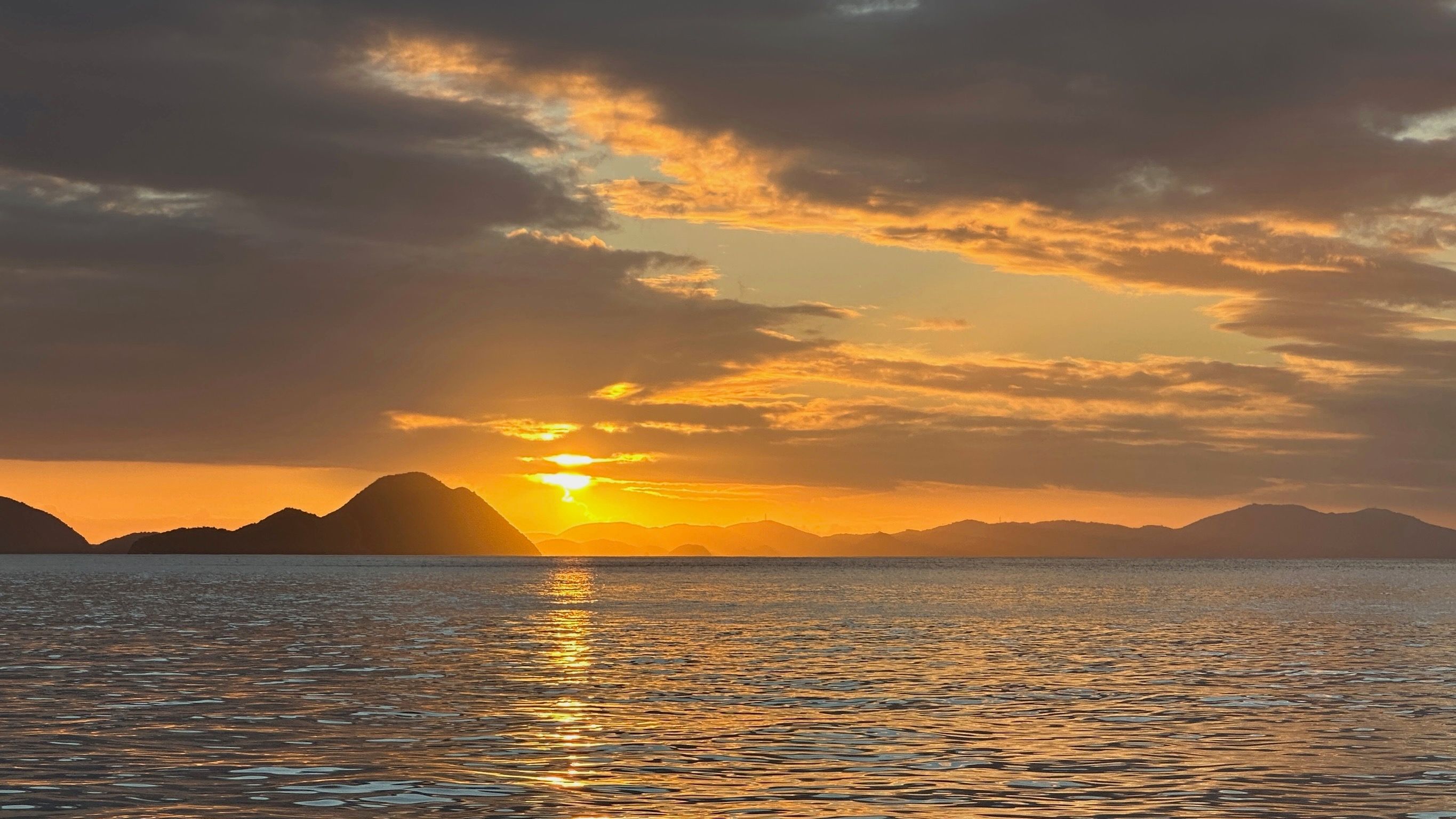 Sonnenuntergang über dem Meer mit dramatischer Wolkenkulisse und silhouettierten Inseln