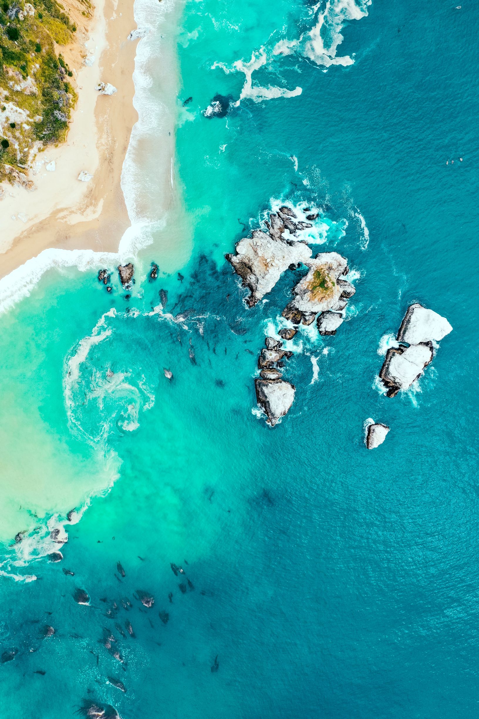 Türkis-blaues Meer mit Strand und Felsen von oben