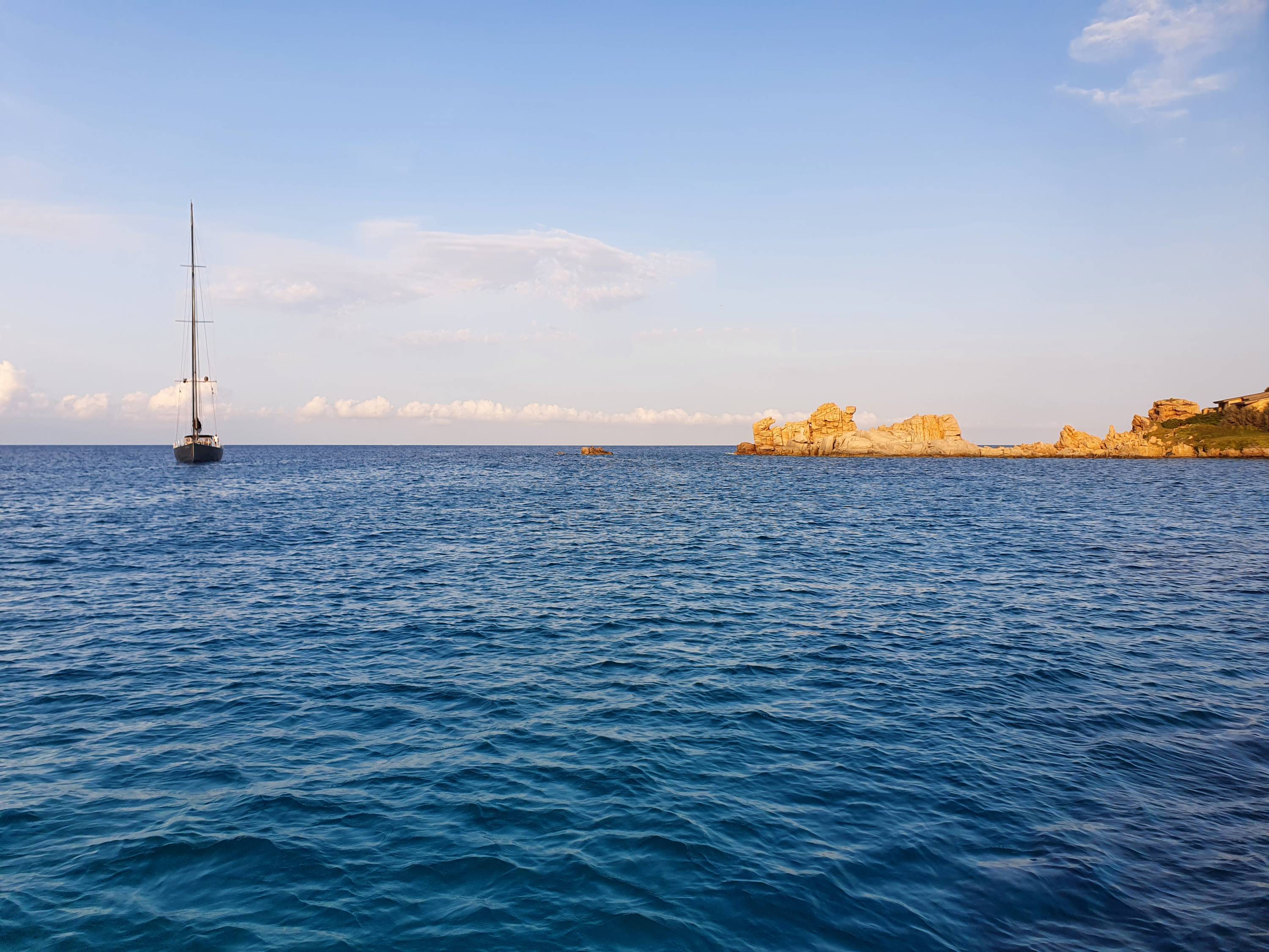 Yacht in der Ferne nebenrotem Felsen im Sonnenuntergang.