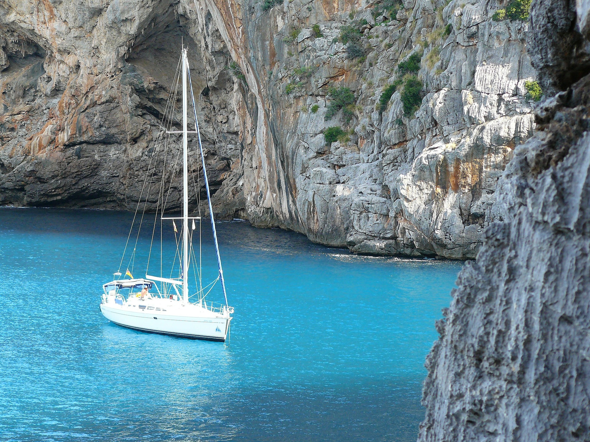 Segelyacht in türkisblauem Wasser vor Anker in einer Felsbucht liegend.