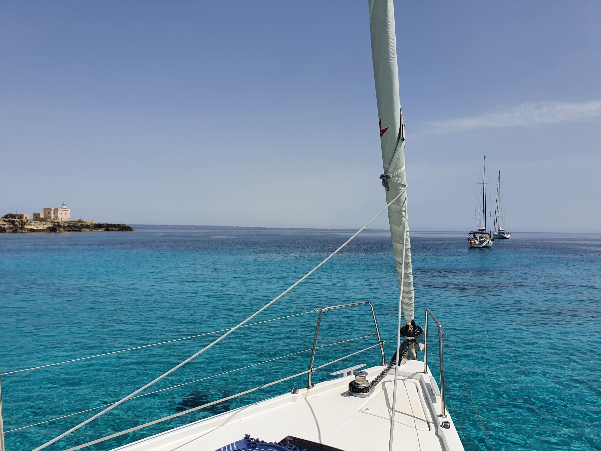 Bug eines Segelschiffes vor Anker in türkisblauer Bucht mit zwei weiteren Yachten im Hintergrund.