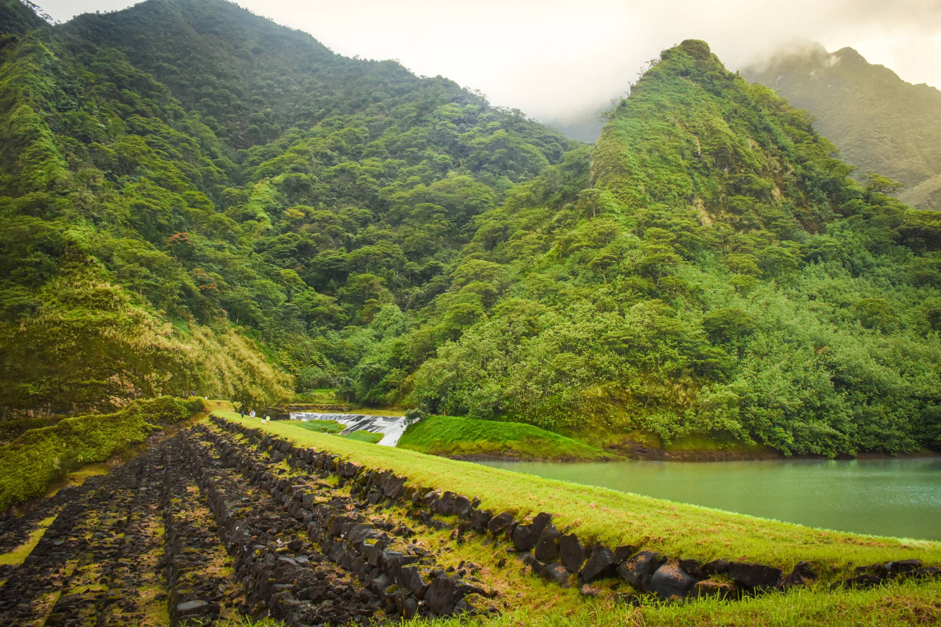 Tropisches Tal mit dichter Vegetation, Flusslauf, Wasserfall und alten Steinmauern im Landesinneren von Tahiti.
