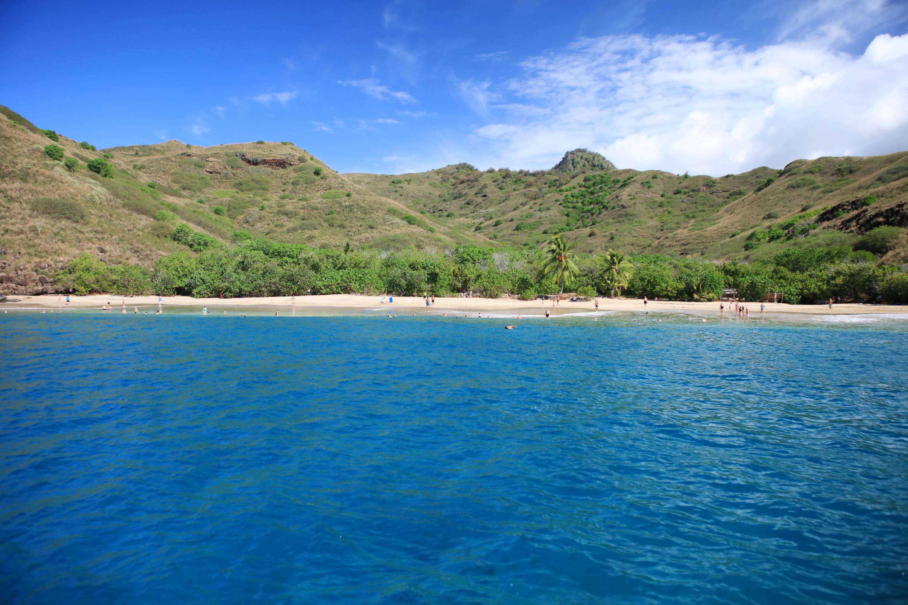 Tropischer Sandstrand auf der Insel Tahuata mit Besuchern im türkisblauen Wasser und grünen Hügeln im Hintergrund.