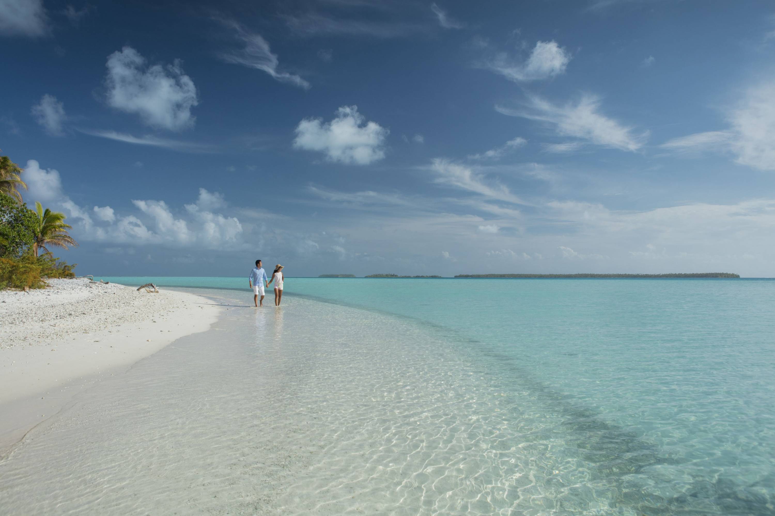 Paar spaziert am weißen Sandstrand von Tetiaroa entlang einer türkisfarbenen Lagune.